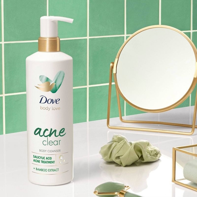 A bottle of acne body wash, a green scrunchie,  a jade roller, and a mirror
