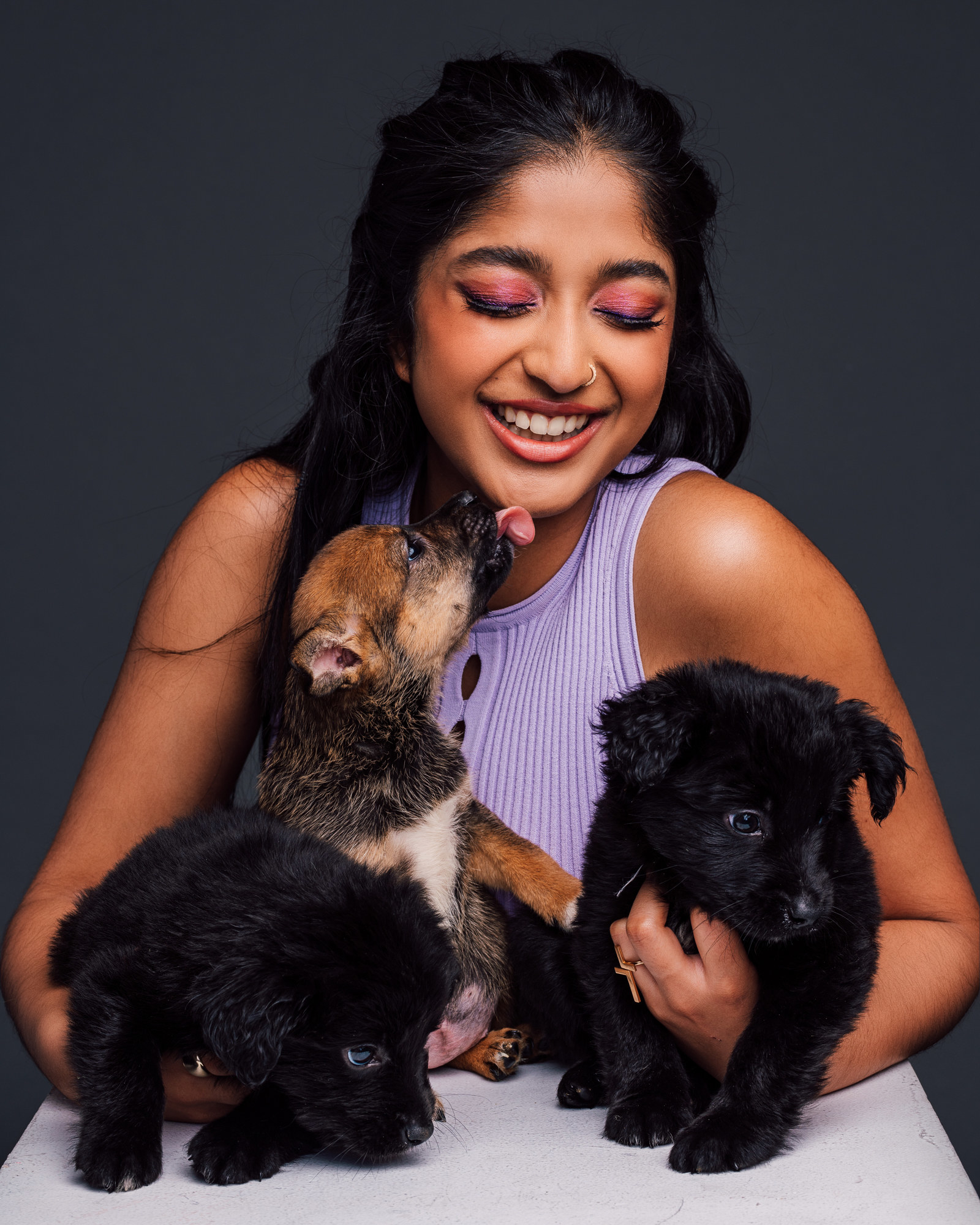Maitreyi smiling and cuddling three adorable puppies as one licks her chin