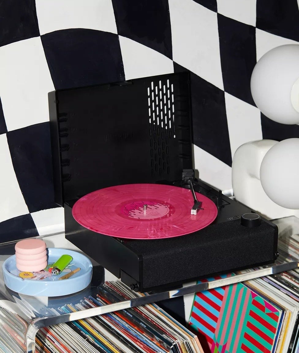 portable black record player on record player stand with vinyls underneath