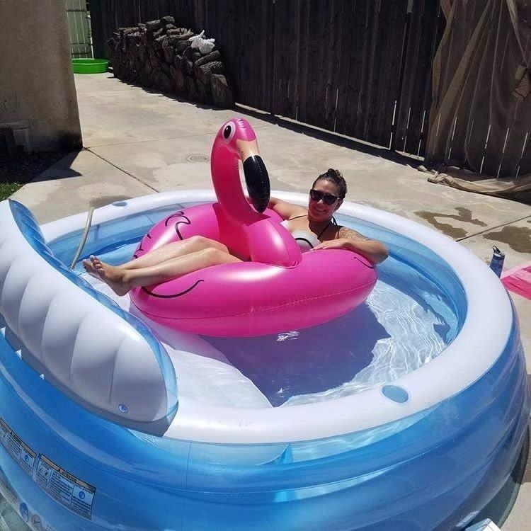 reviewer sitting in flamingo pool float inside inflatable pool