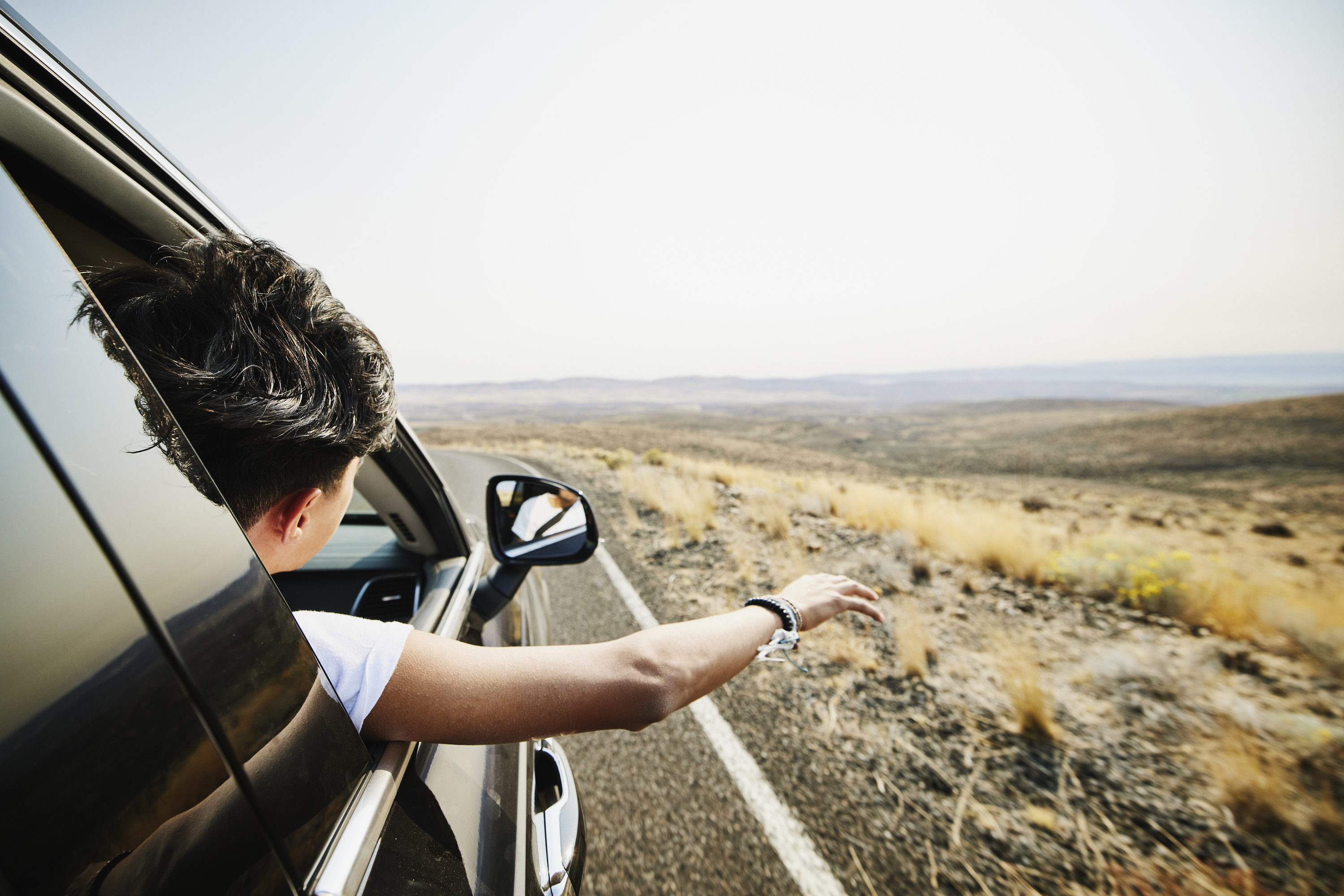 teen with hand out window on road trip