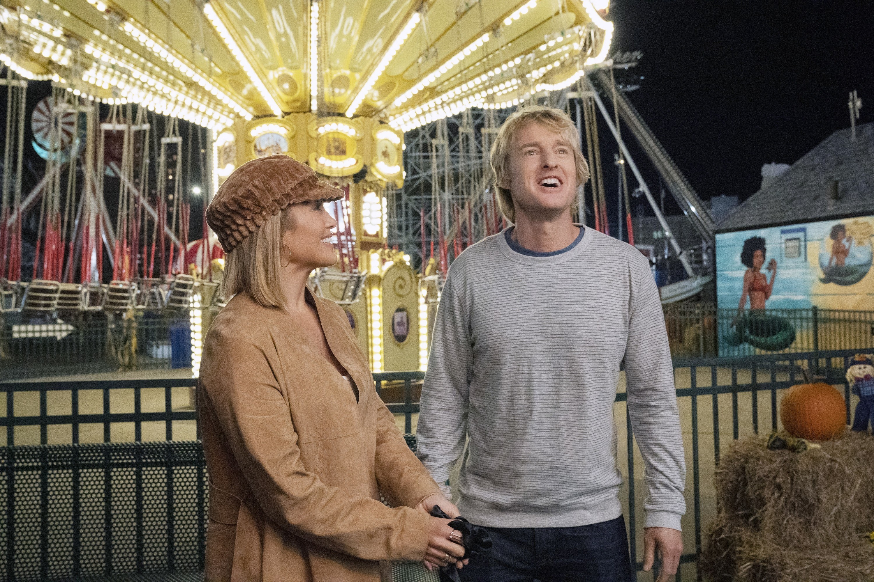 Jennifer Lopez and Owen Wilson standing next to a swings ride in Marry Me