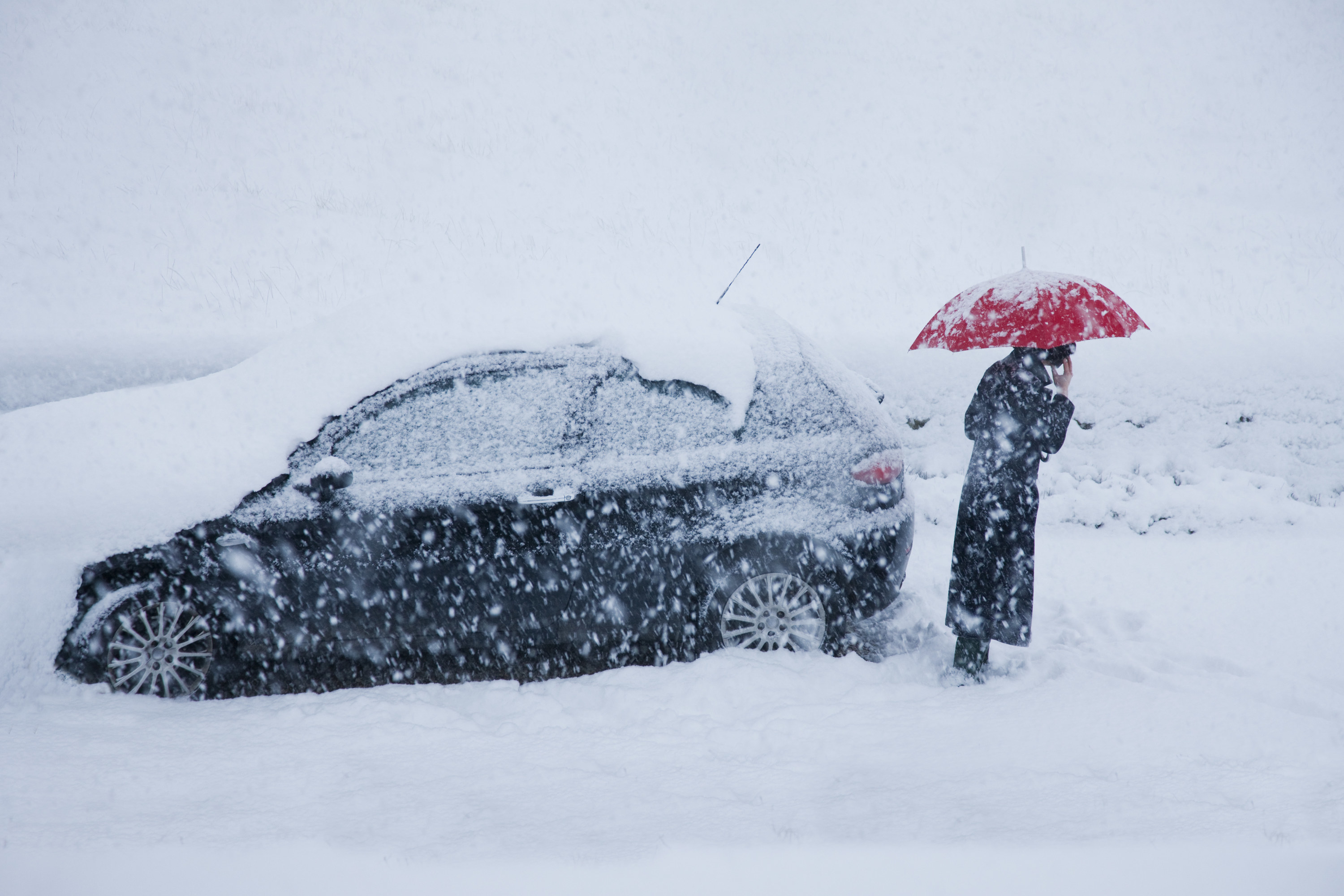 a car in a snowstorm with a person and an umbrella