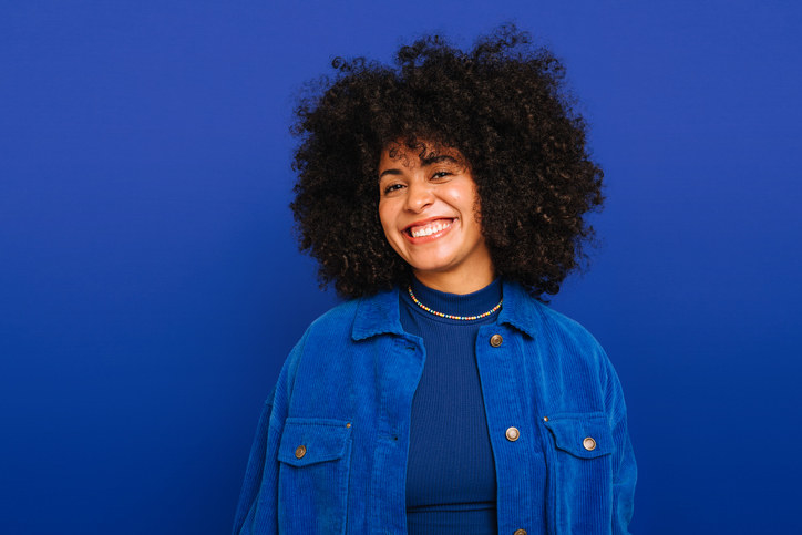 A young woman smiling in a blue shirt and jacket, with a blue background behind her