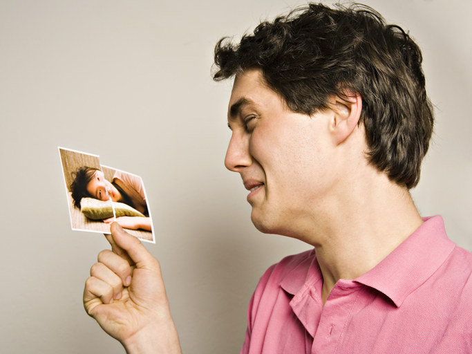A man crying and looking at a ripped up picture of their ex