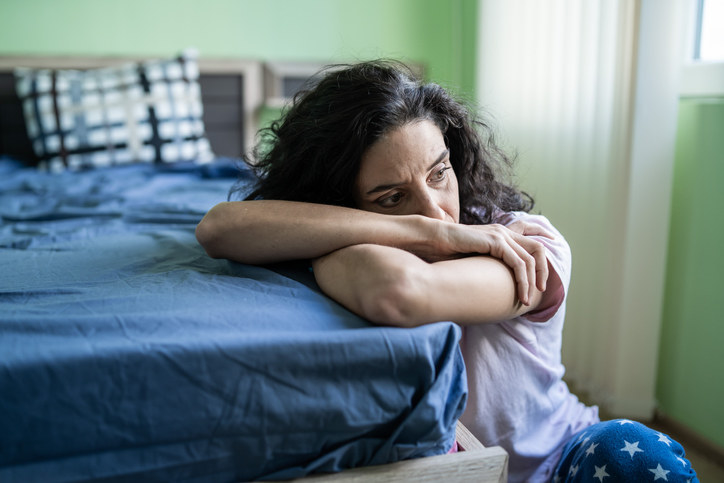 A woman looking sad, with her head and arms on the edge of her bed