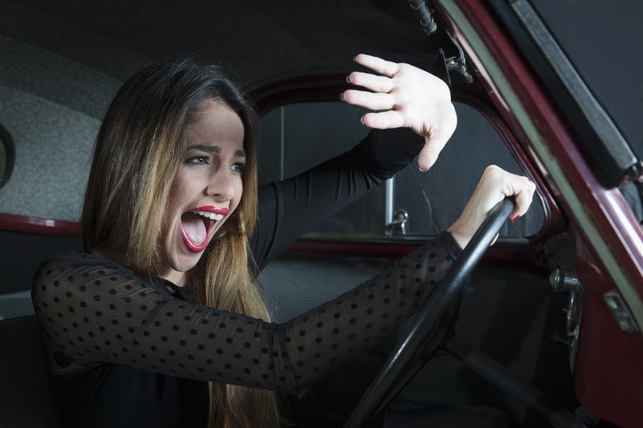 A woman who is driving and screaming, while holding up her hands to block out some blinding lights