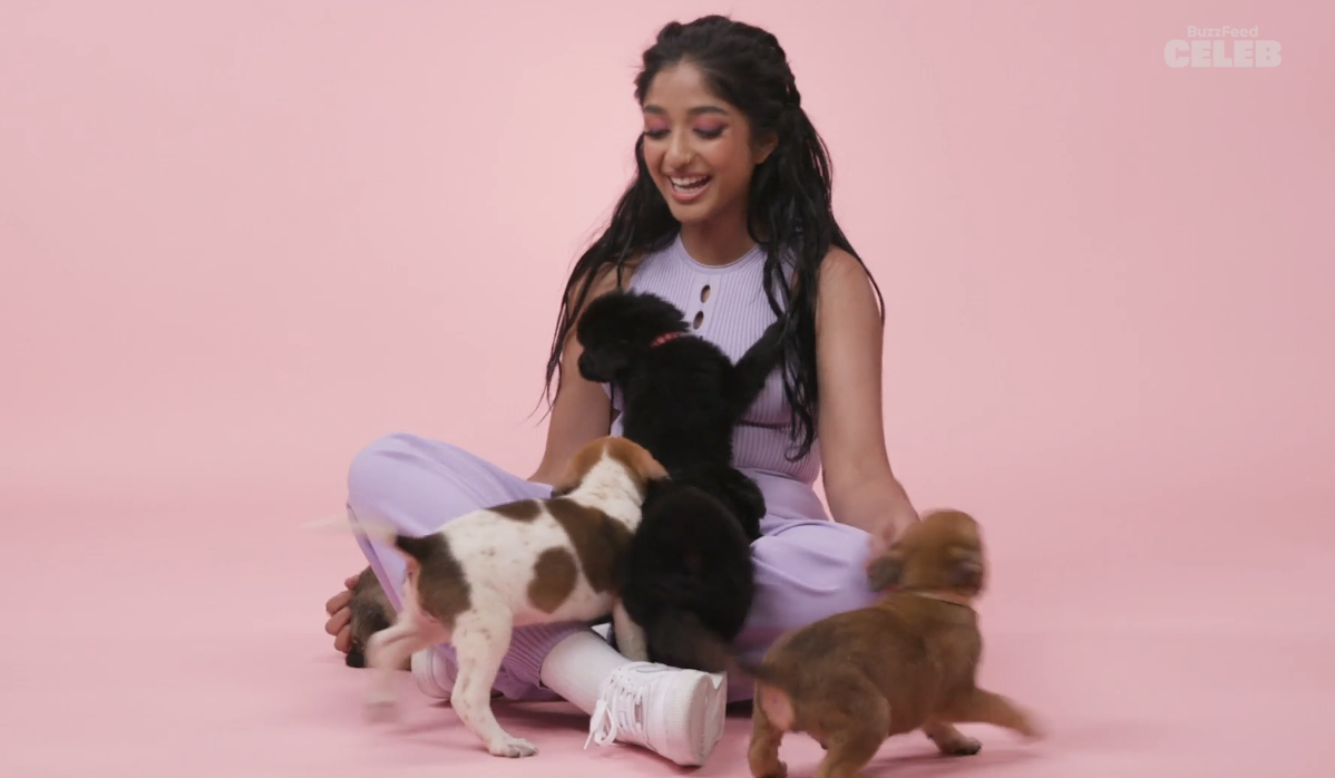 Maitreyi sitting cross-legged and playing with puppies and smiling