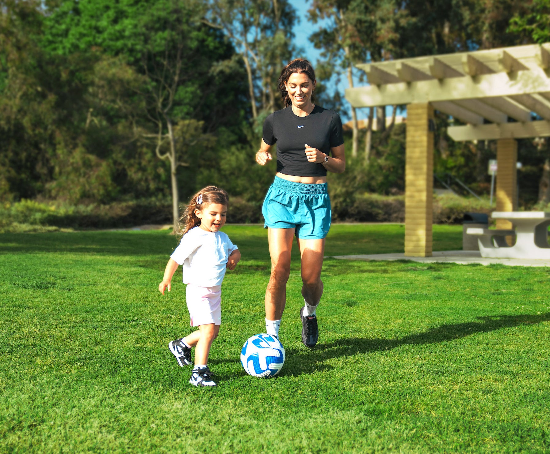 Close up of Alex Morgan and her daughter Charlie kick a soccer ball in the backyard