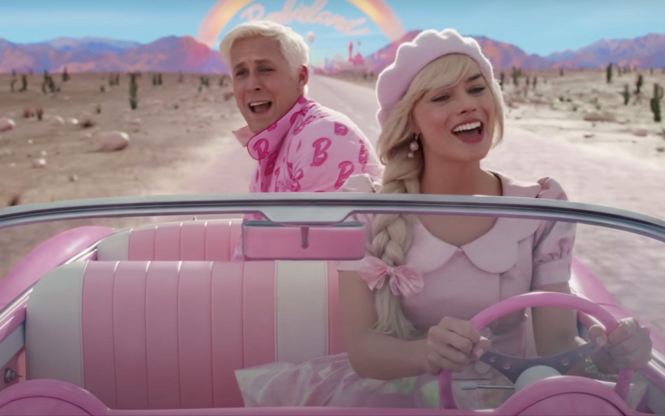 Margot as Barbie driving a pink car and Ken pops up in the back seat