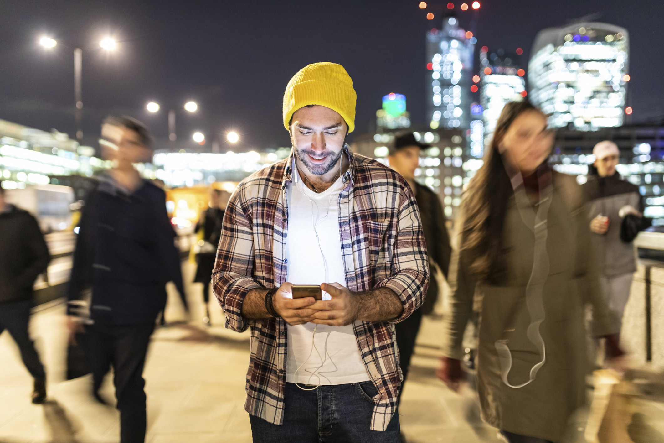 A man in a crowd on the street checking his cellphone and wearing headphones