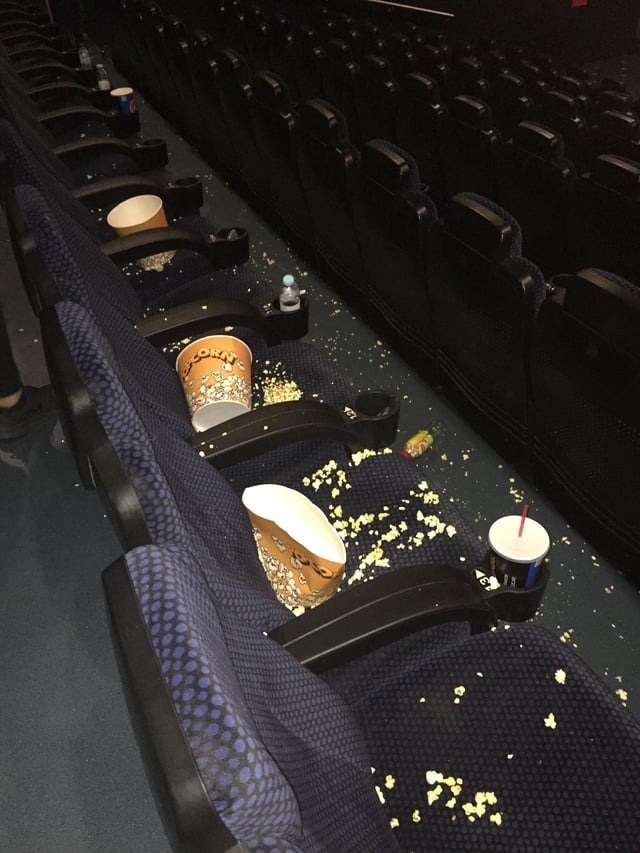Popcorn and popcorn buckets and drink cups left in the seats and on the floor of a movie theater
