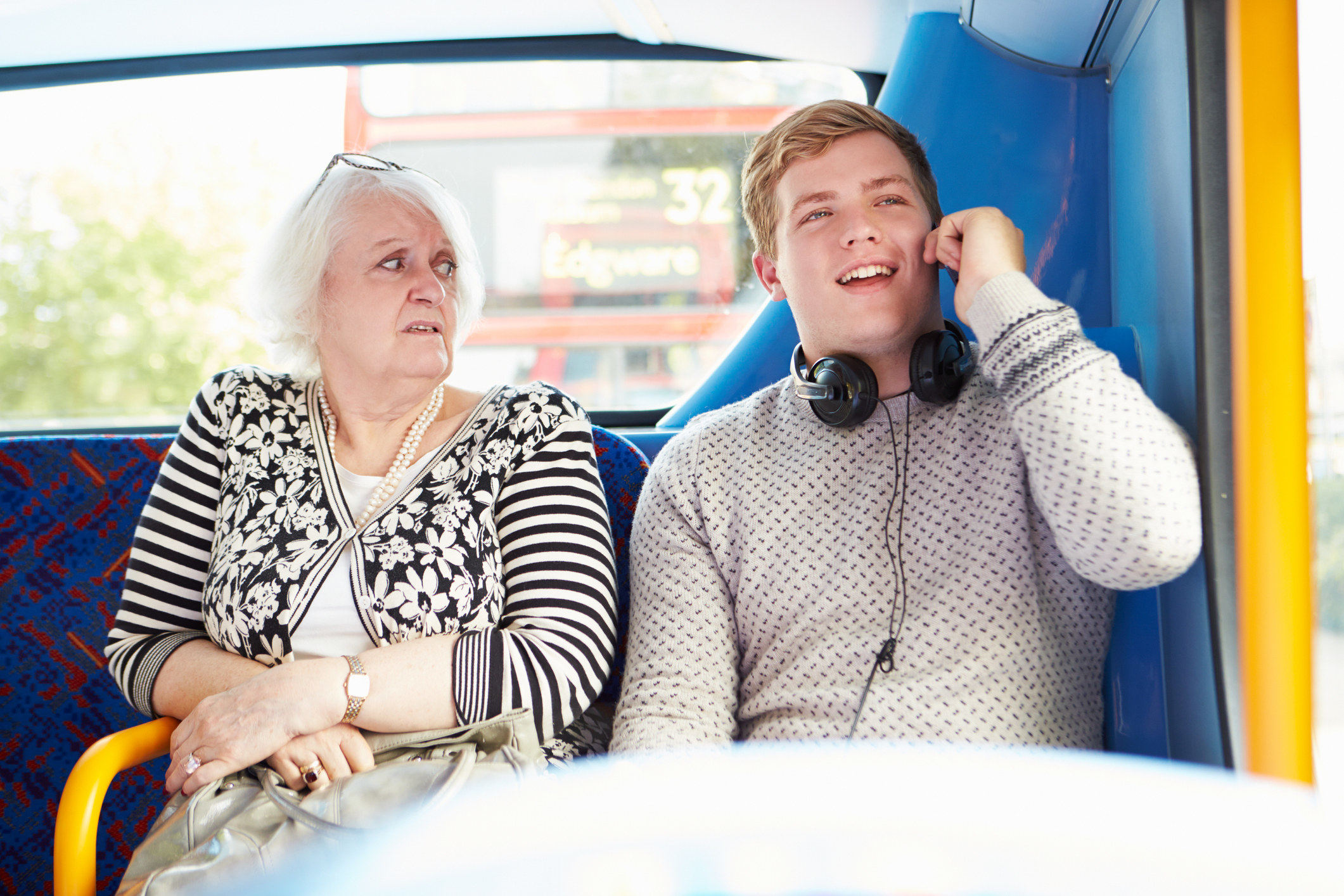 A woman looking in disgust at a young man wearing headphones on the bus