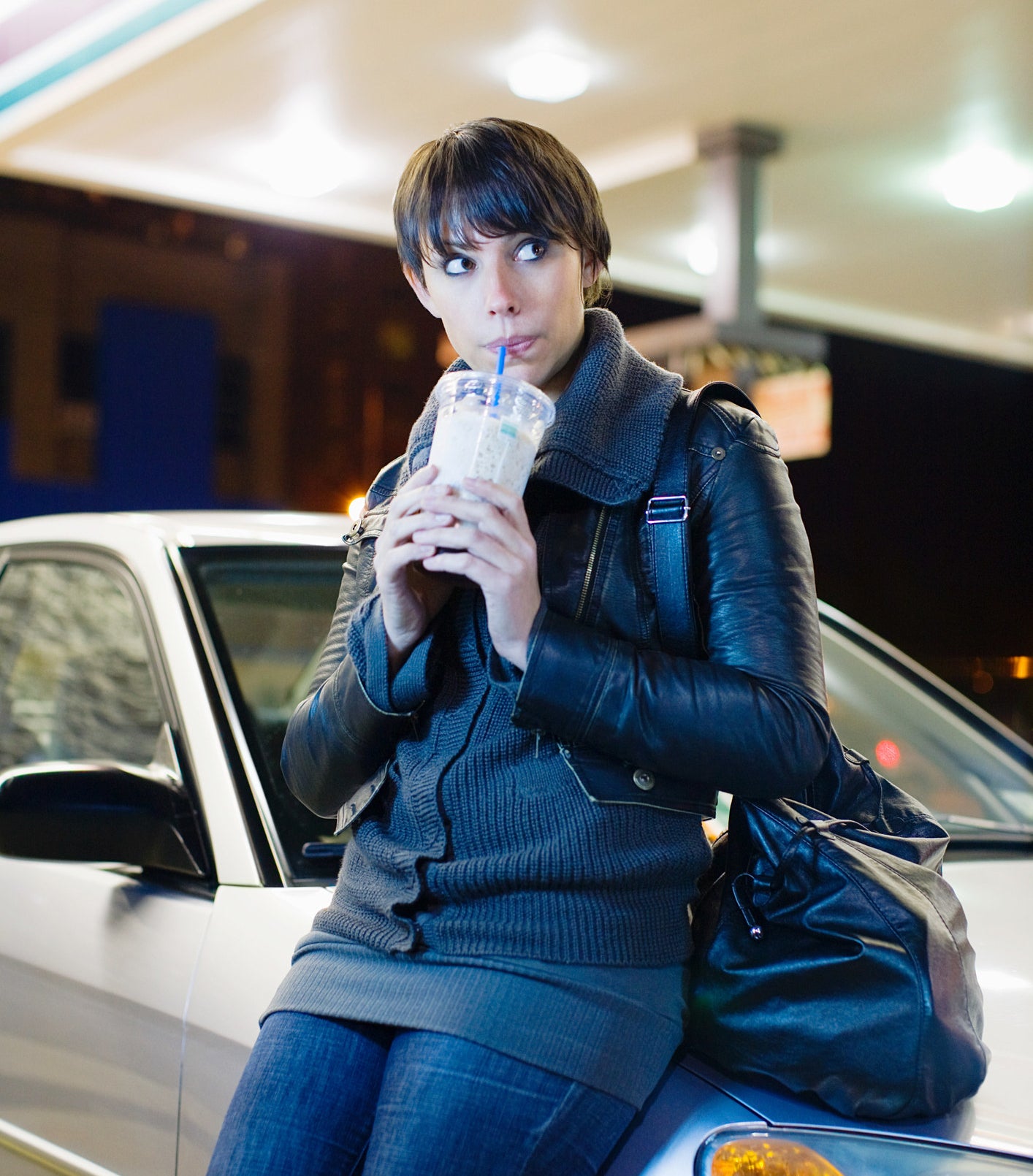 A person drinking a beverage while leaning on a car