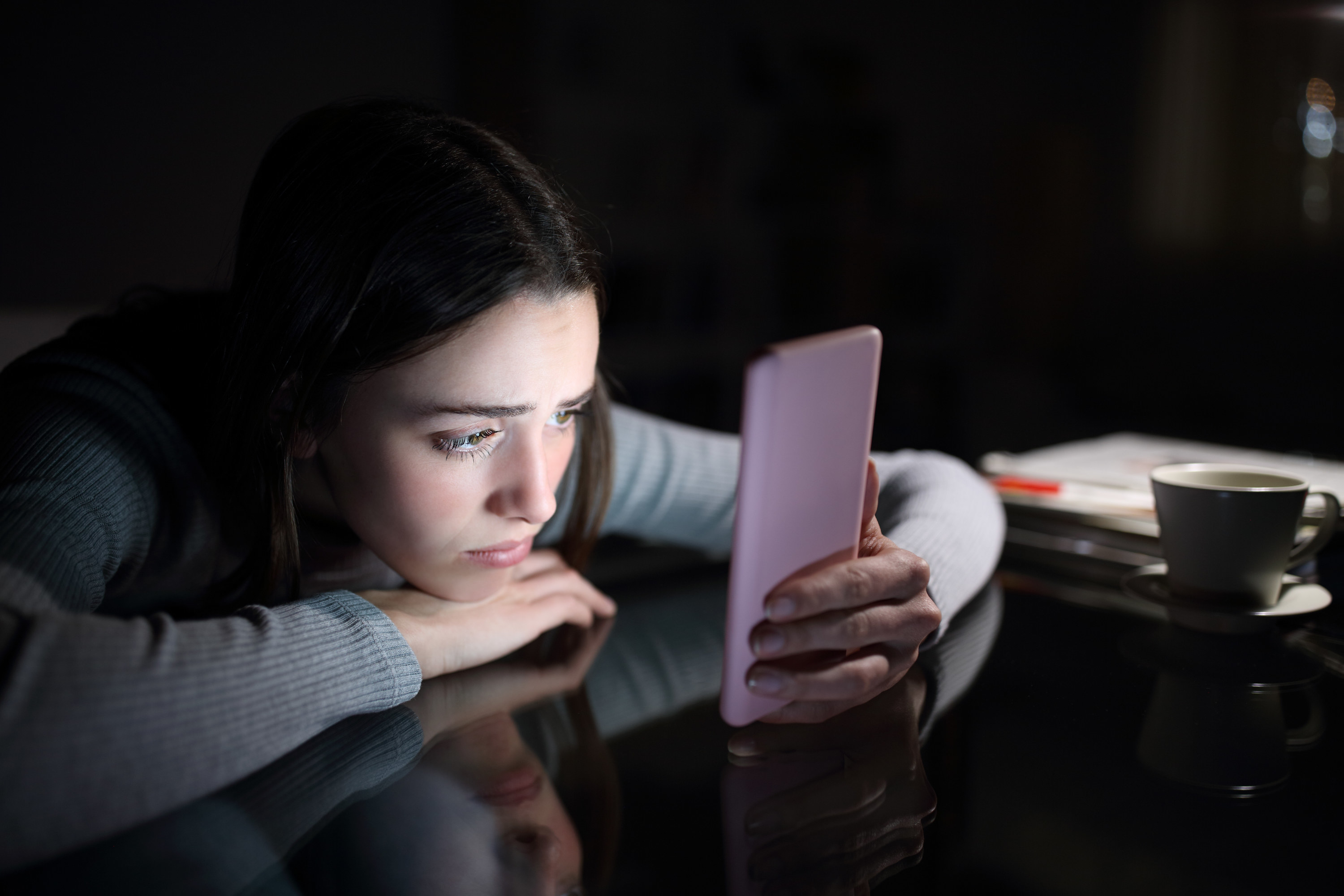 A girl looks sad while staring at her phone in the dark