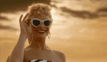 Margot Robbie smiling and peering over her sunglasses in the "Barbie" movie