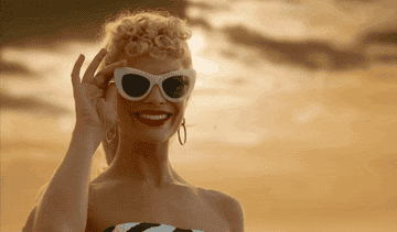 Margot Robbie smiling and peering over her sunglasses in the &quot;Barbie&quot; movie