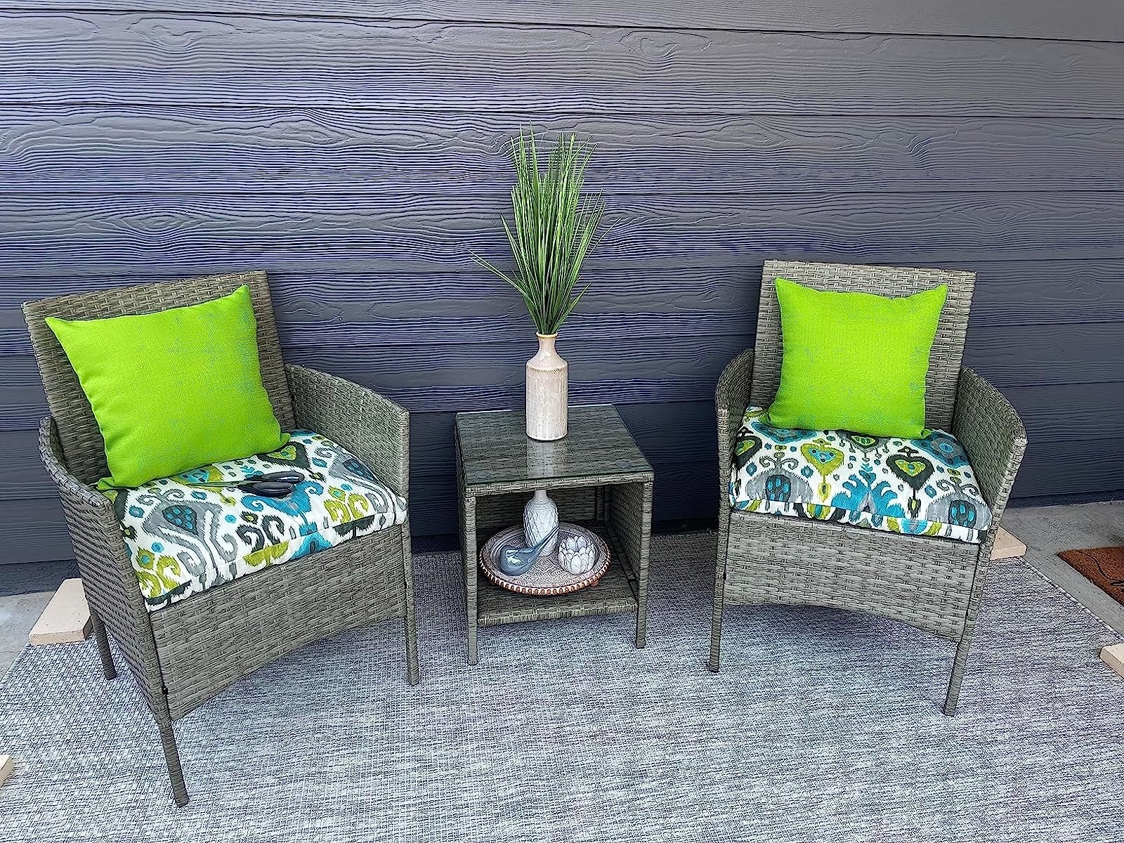 Reviewer image of the two chairs and small side table on their patio with colorful cushions on them
