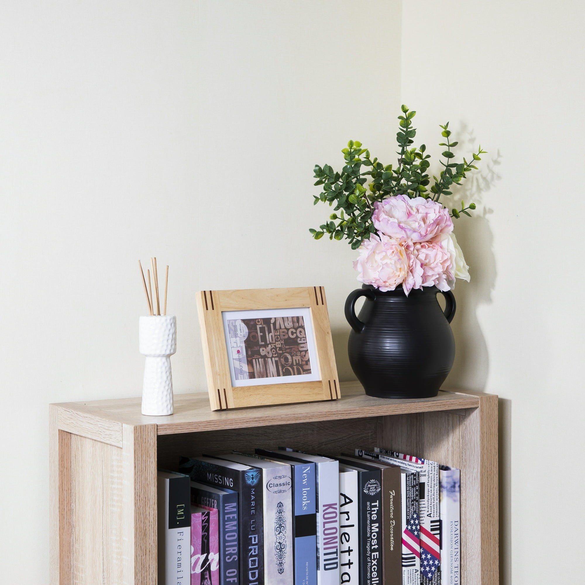 black round vase with pink flowers on top of bookcase