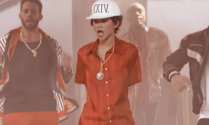 Zendaya dress in a shirt, chain, and cap and she impersonates Bruno Mars