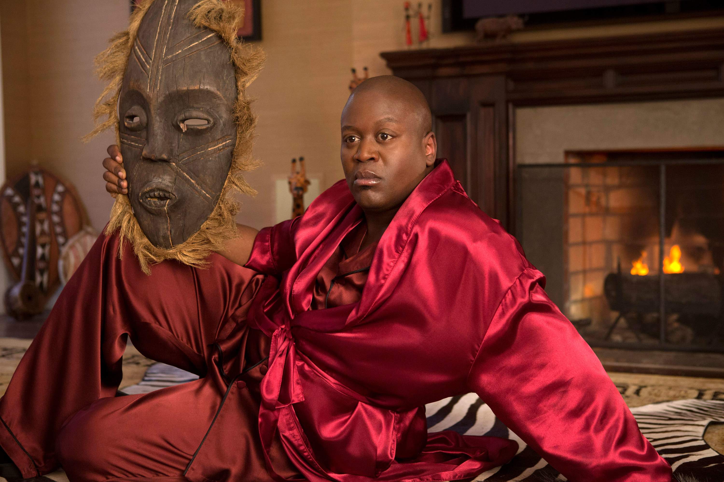 titus posing in silk pyjamas and holding a large african mask