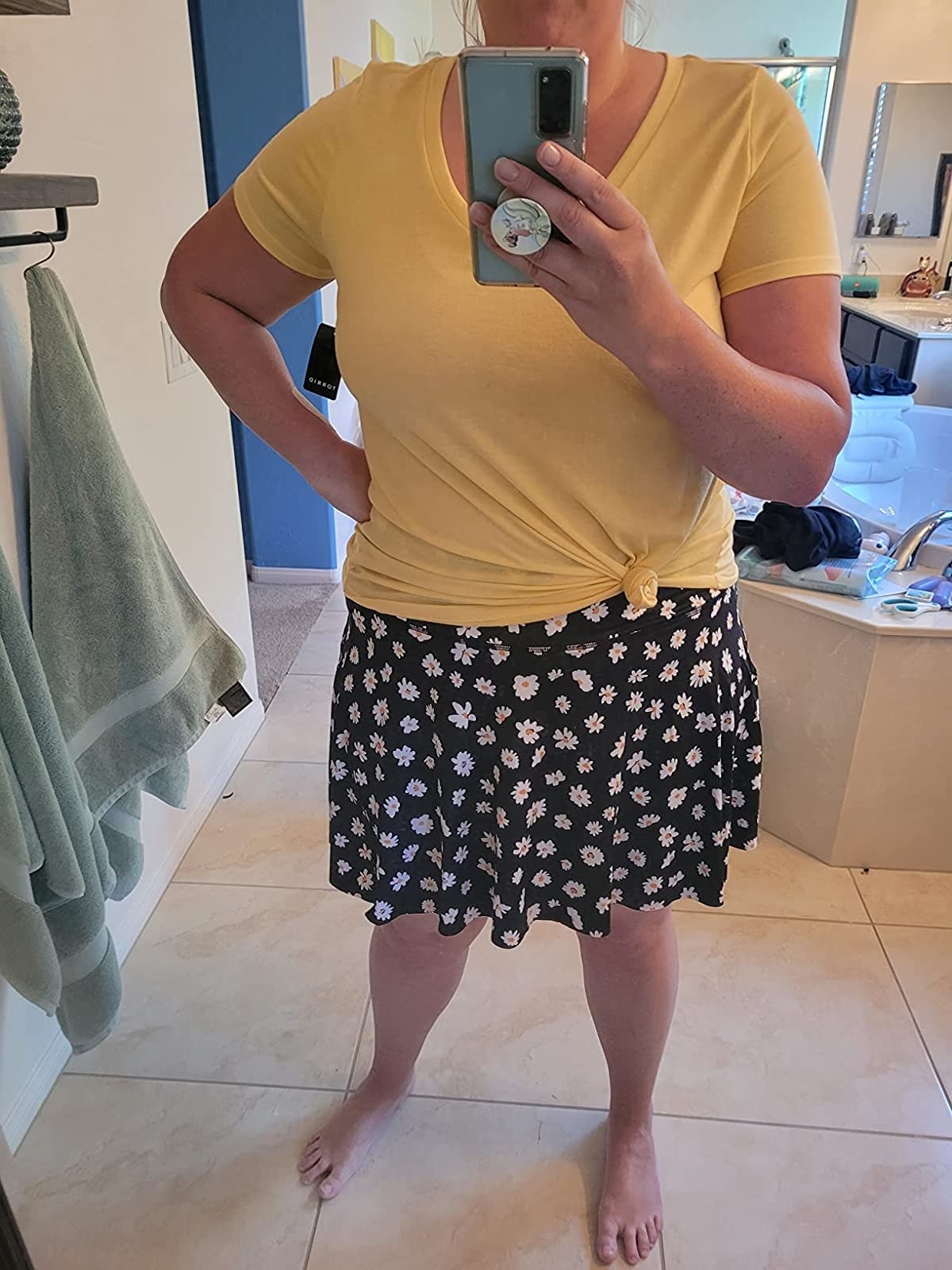 A reviewer wearing a yellow top with blue skort with yellow and white daisies