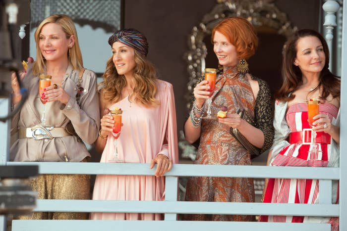 The four cast members sip drinks on a balcony while filming