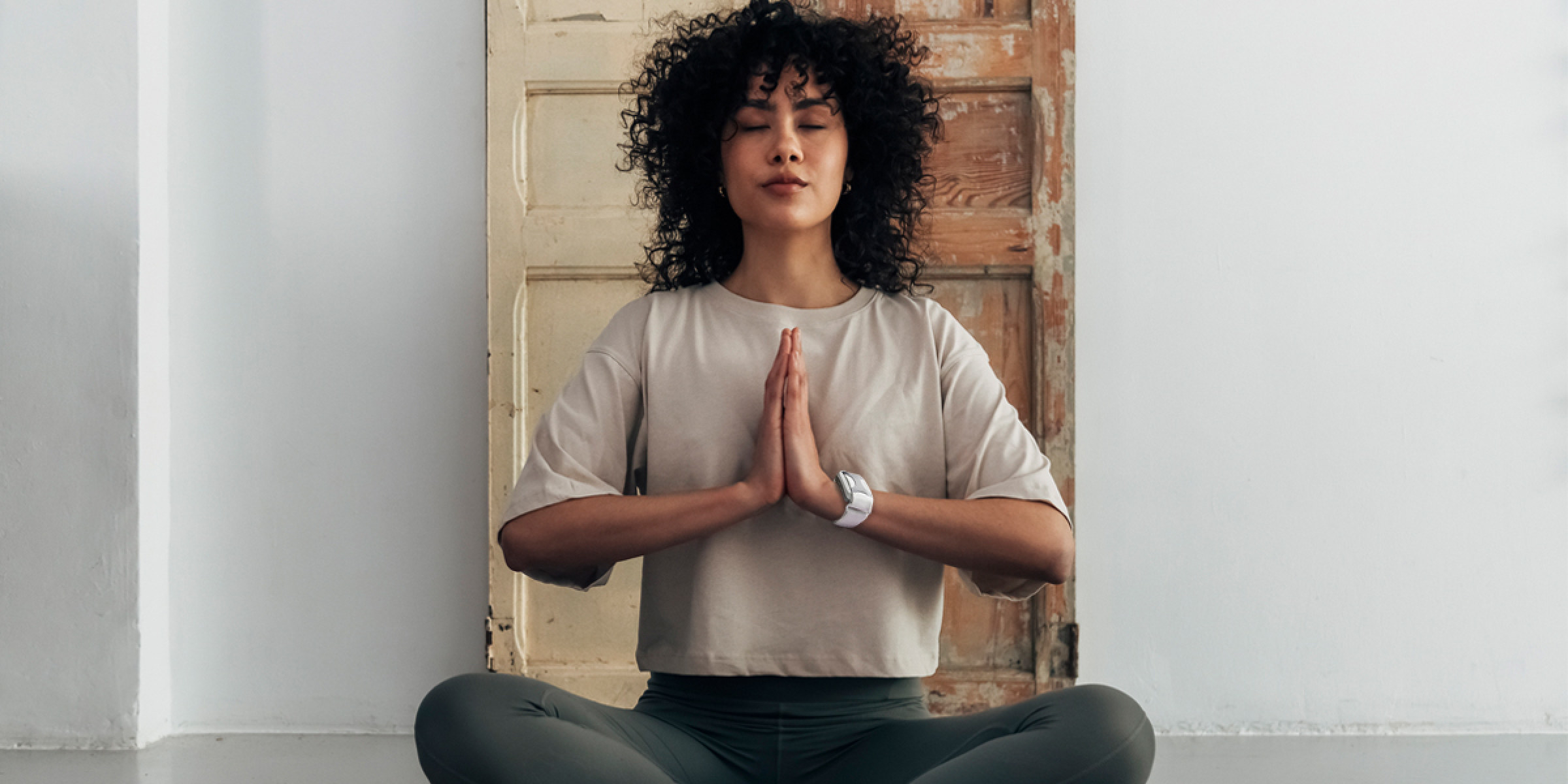 A woman sits in a yoga pose wearing Apollo Neuro