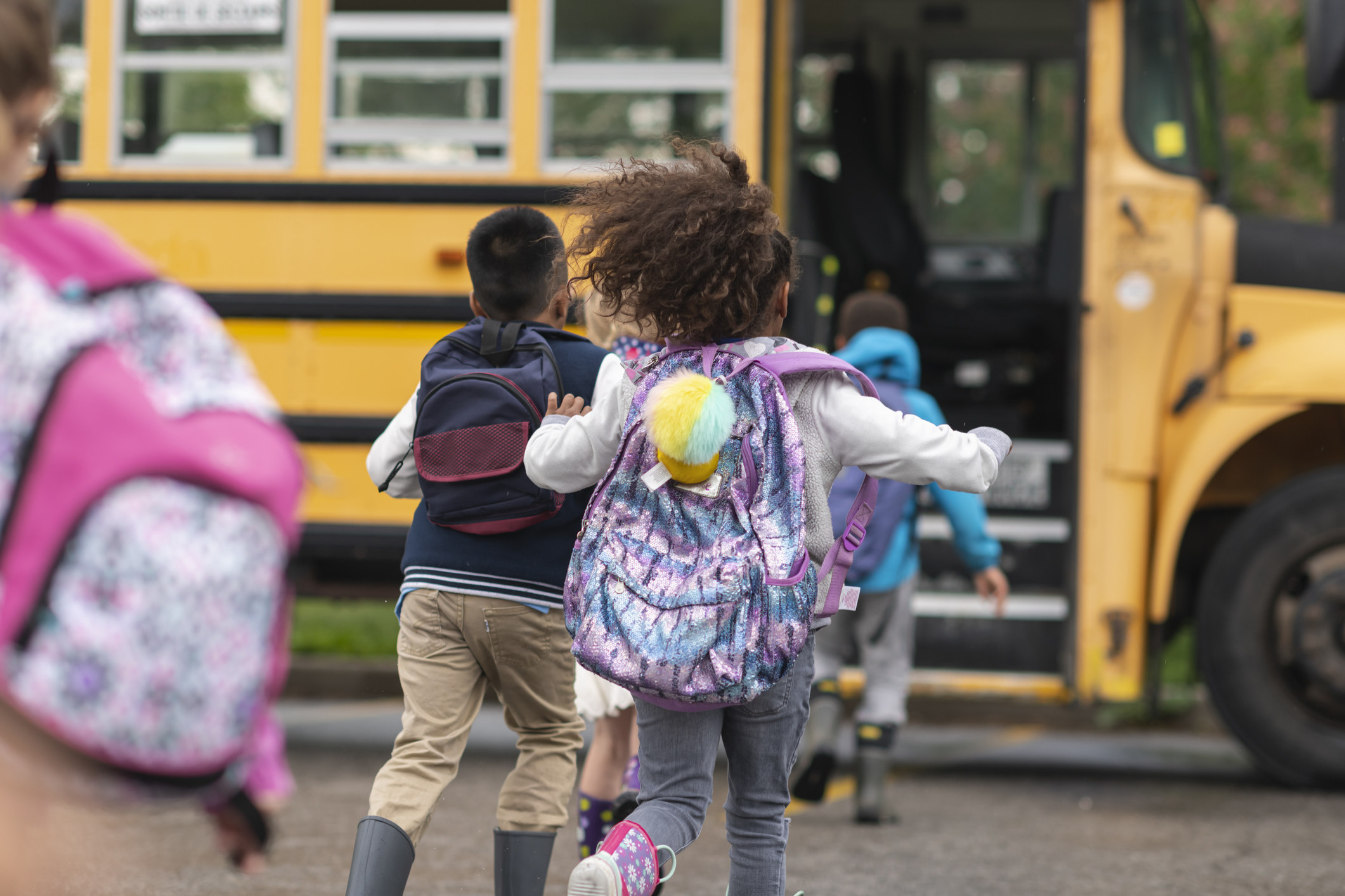 Kids running to a yellow school bus.