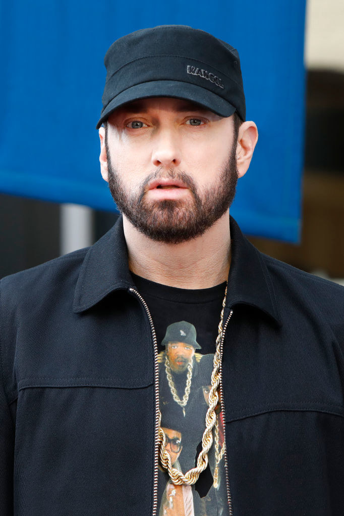A close-up of a bearded Eminem wearing a Run DMC t-shirt, a chain, and a jacket