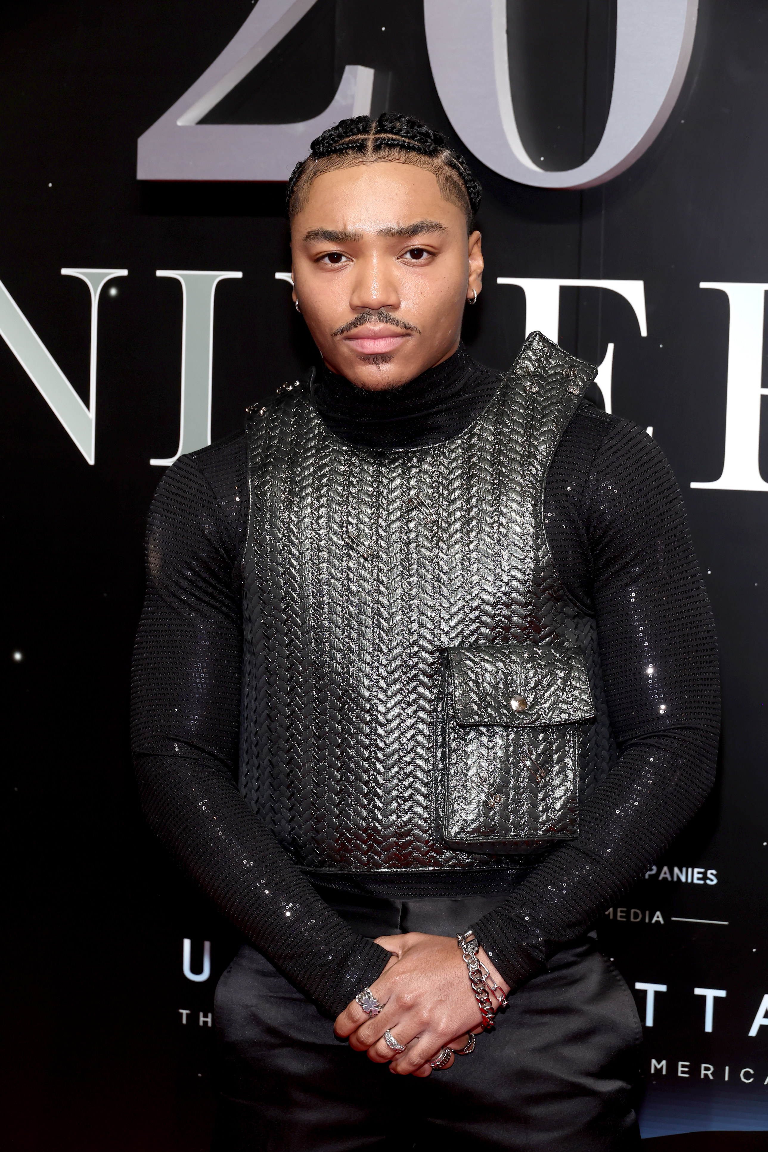 A close-up of Josh Levi posing for photographers on the red carpet. Josh is wearing a sequined long-sleeve shirt and a textured top that emulates a bulletproof vest