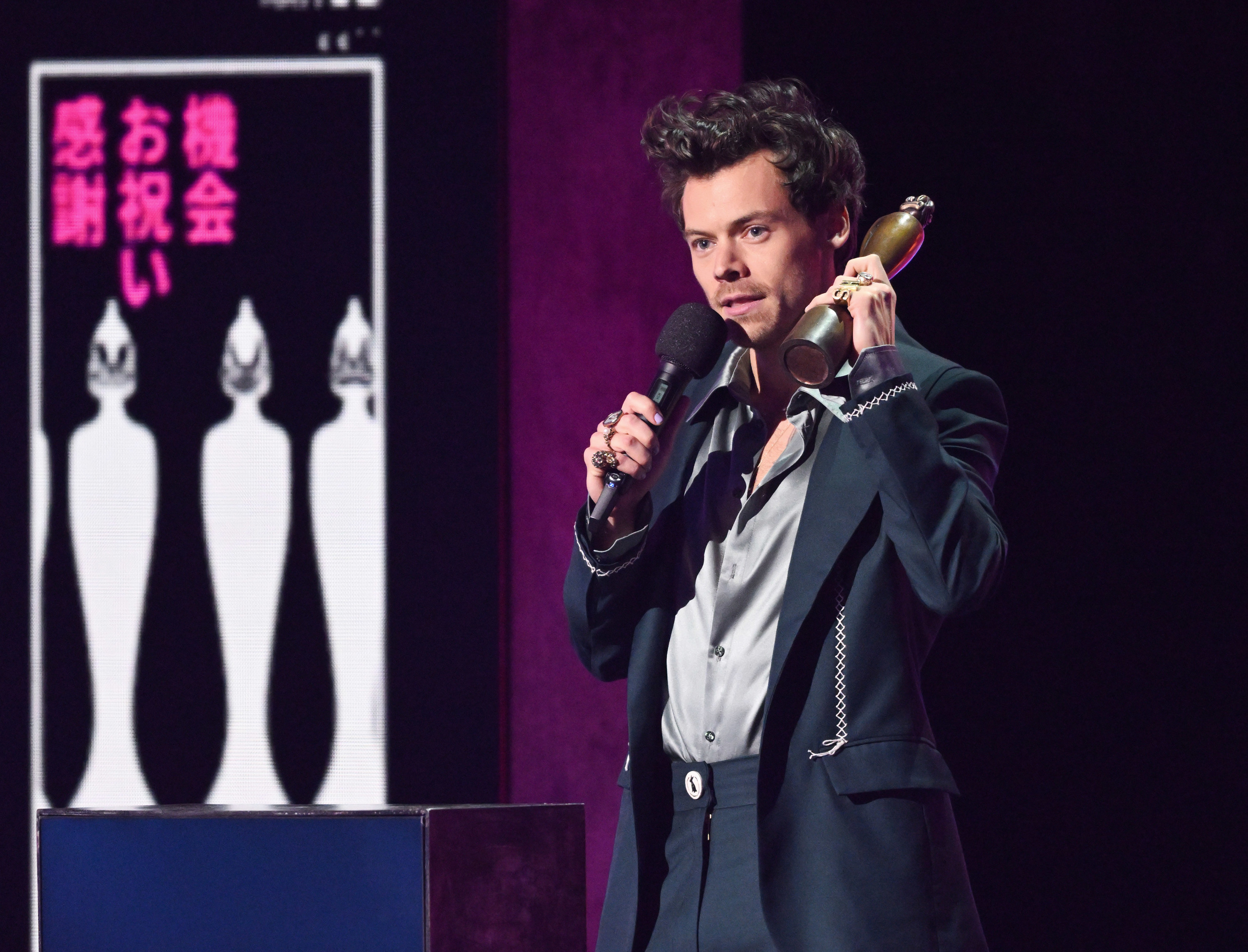 Harry Styles onstage holding a microphone and an award