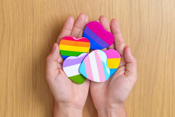 Hands holding hearts with various LGBTQIA+ community flags
