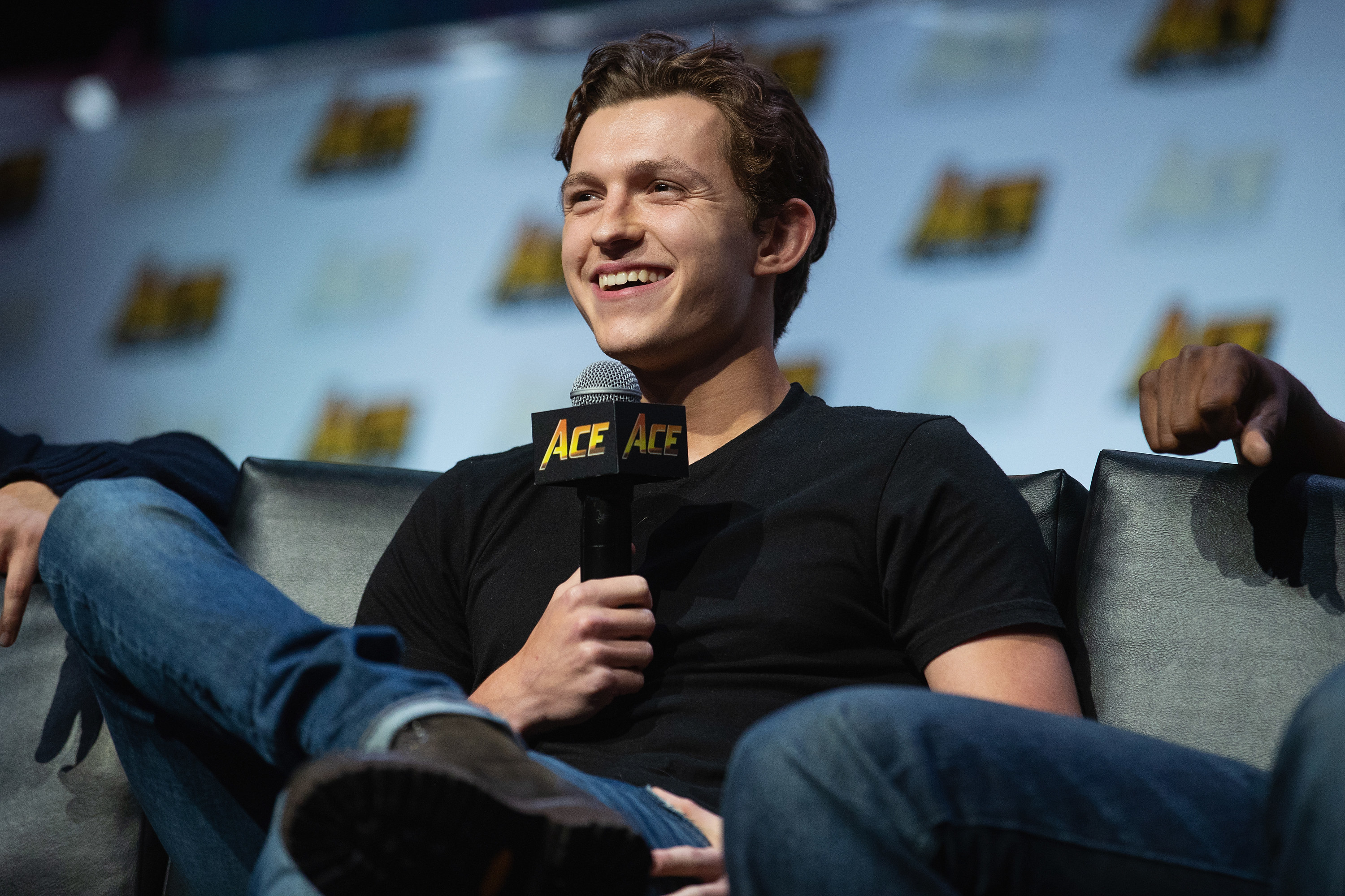 Tom smiling and sitting holding a microphone