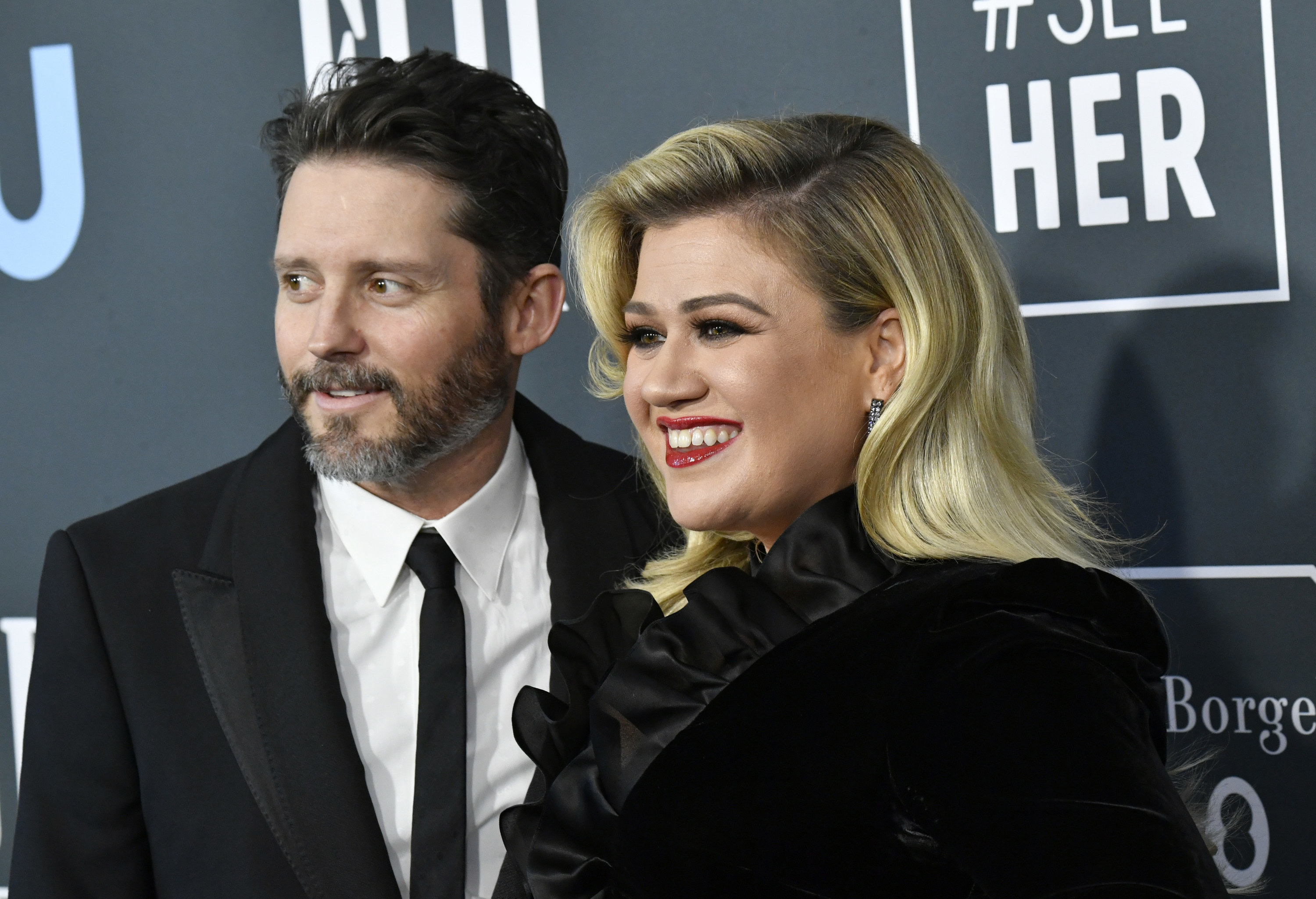 Close-up of Brandon, smiling in a suit and tie, and a smiling Kelly, in a frilly-collar outfit