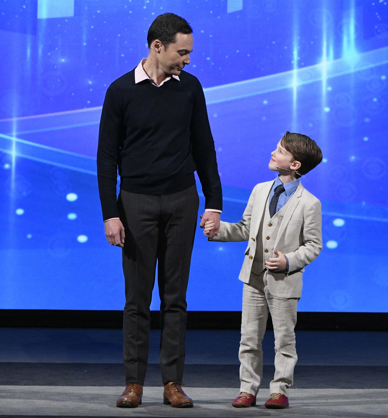 jim parsons and young iain armitage holding hands on a stage