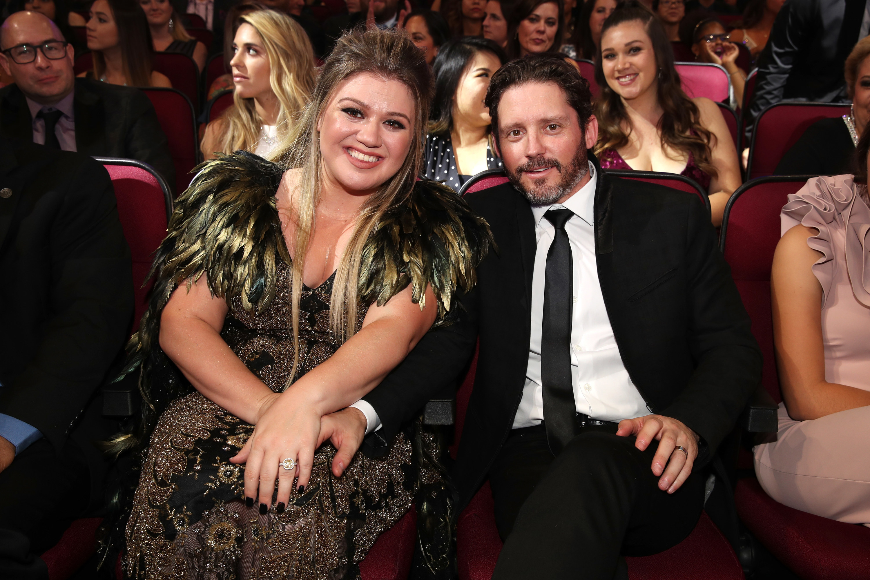 Kelly and Brandon sitting together in an audience and smiling, with Brandon&#x27;s hand touching Kelly&#x27;s knee