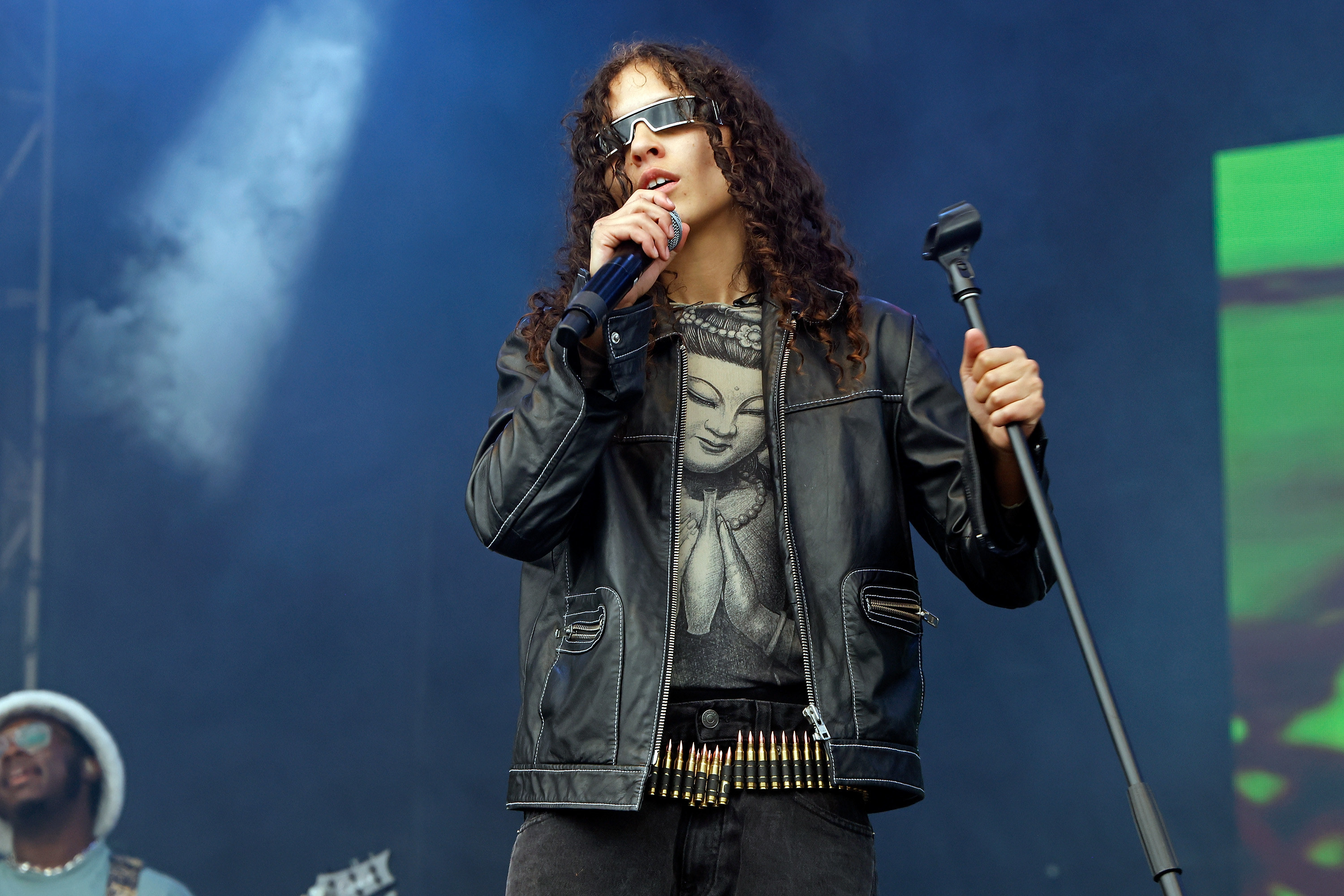 070 Shake performing onstage and wearing a jacket and bullet belt