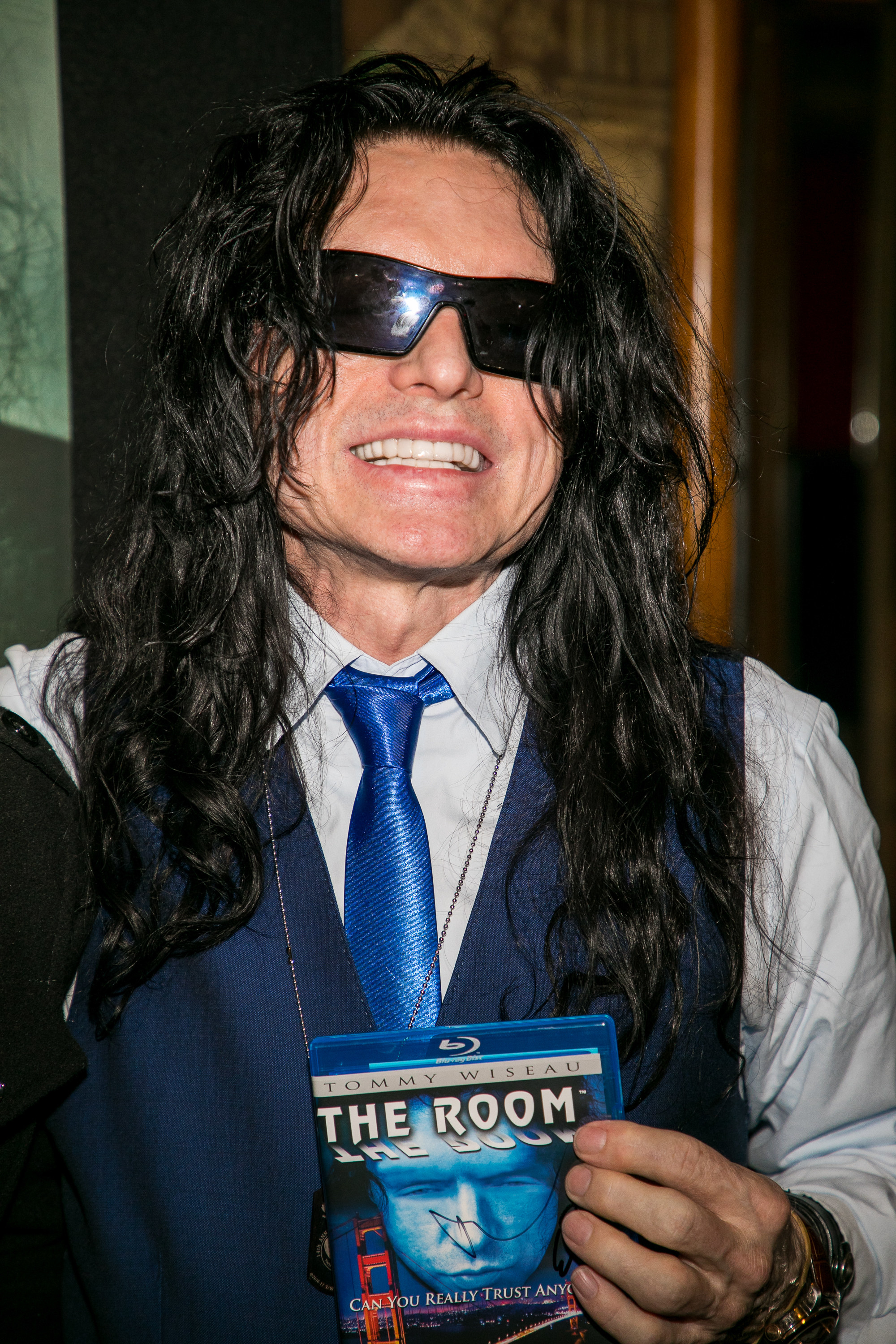 Tommy Wiseau smiling and holding a blu-ray copy of The Room