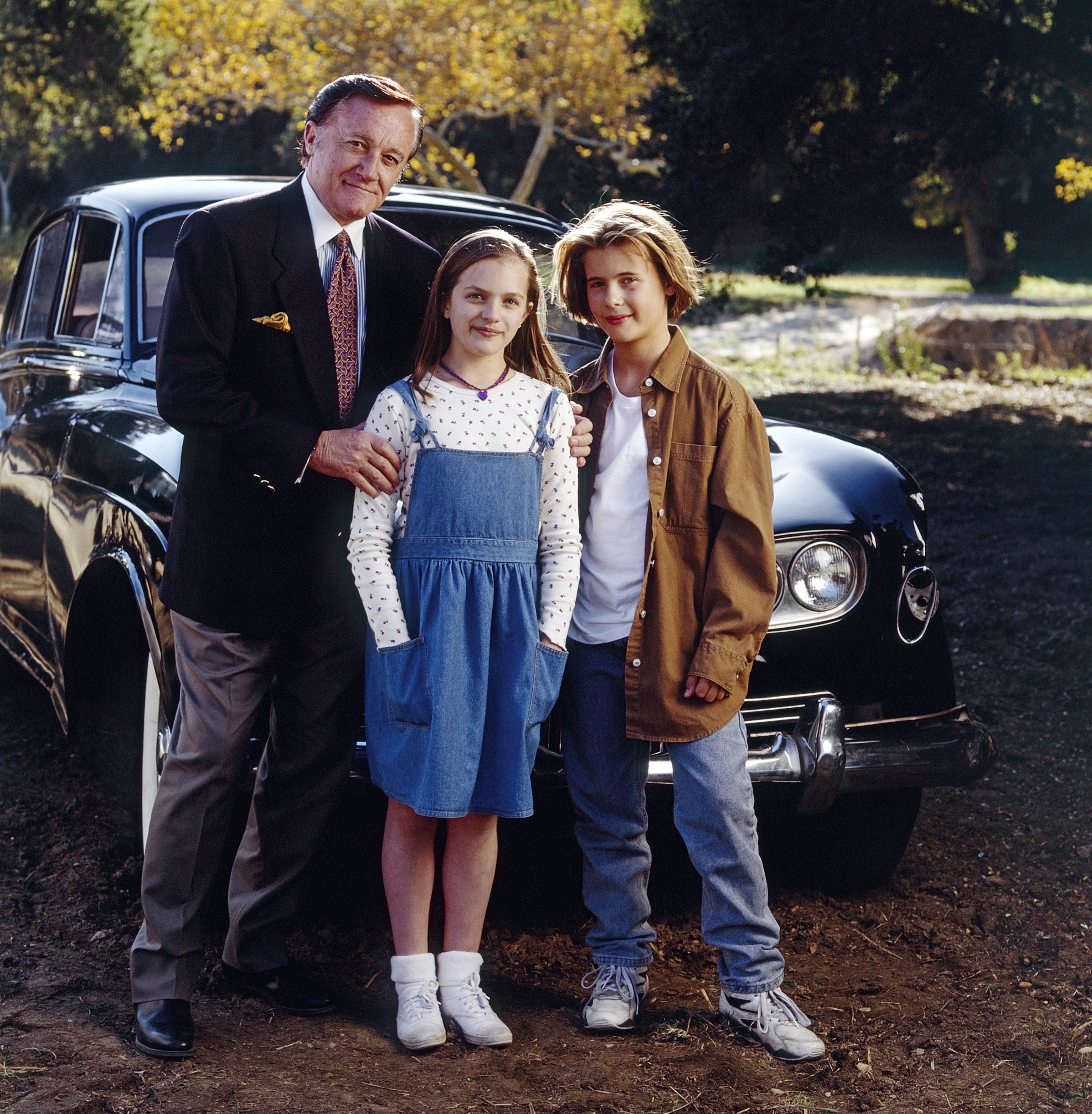 man and two pre-teens standing in front of a car