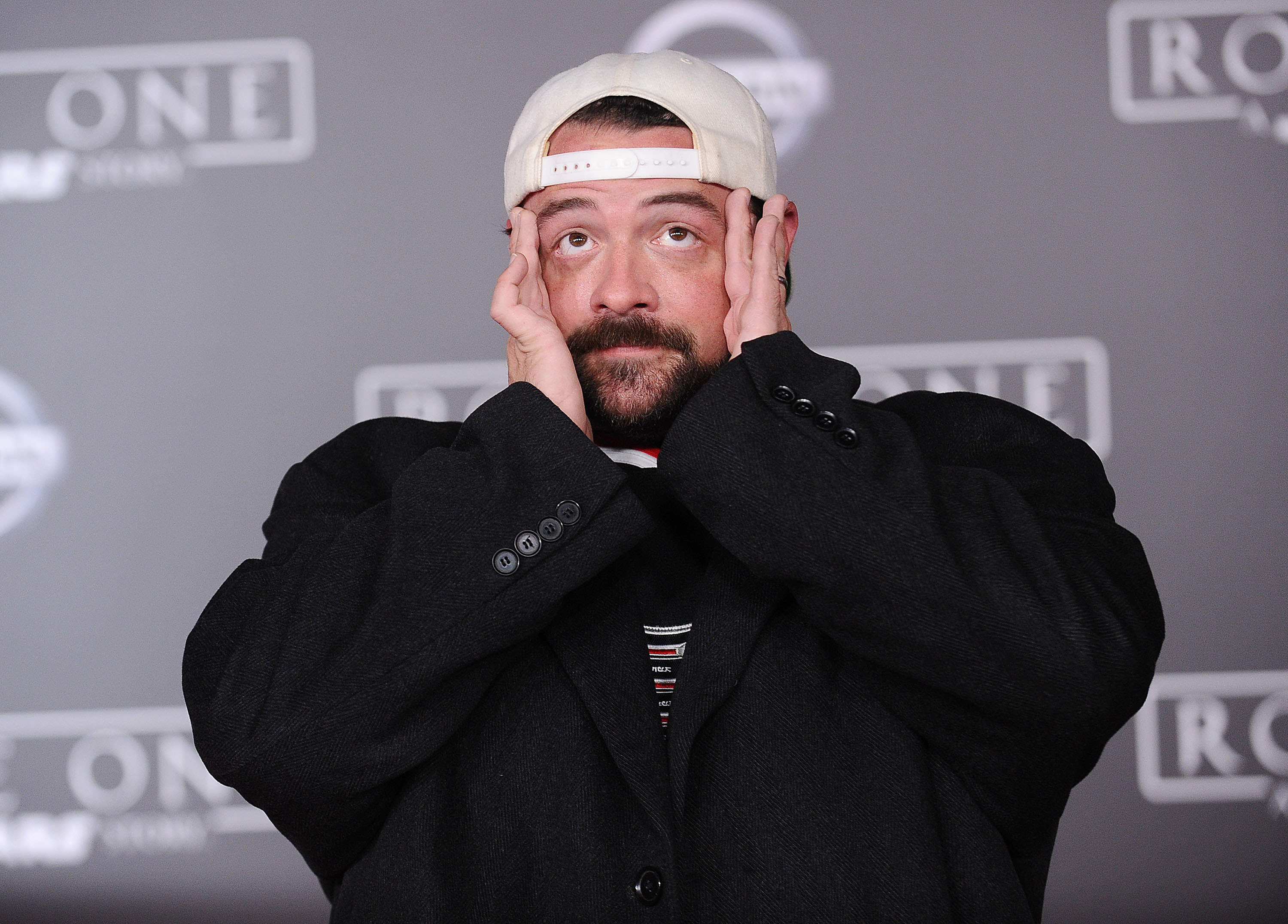 Kevin Smith posing on a red carpet with his hands on his head