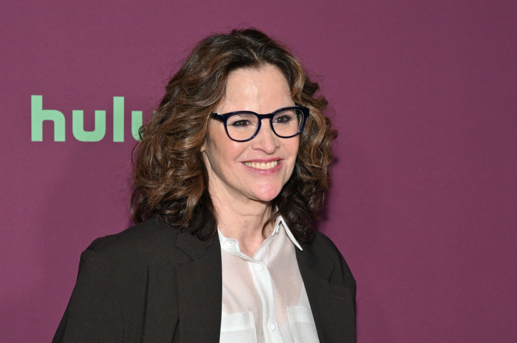 Close-up of Ally smiling and wearing glasses, a blouse, and a suit jacket