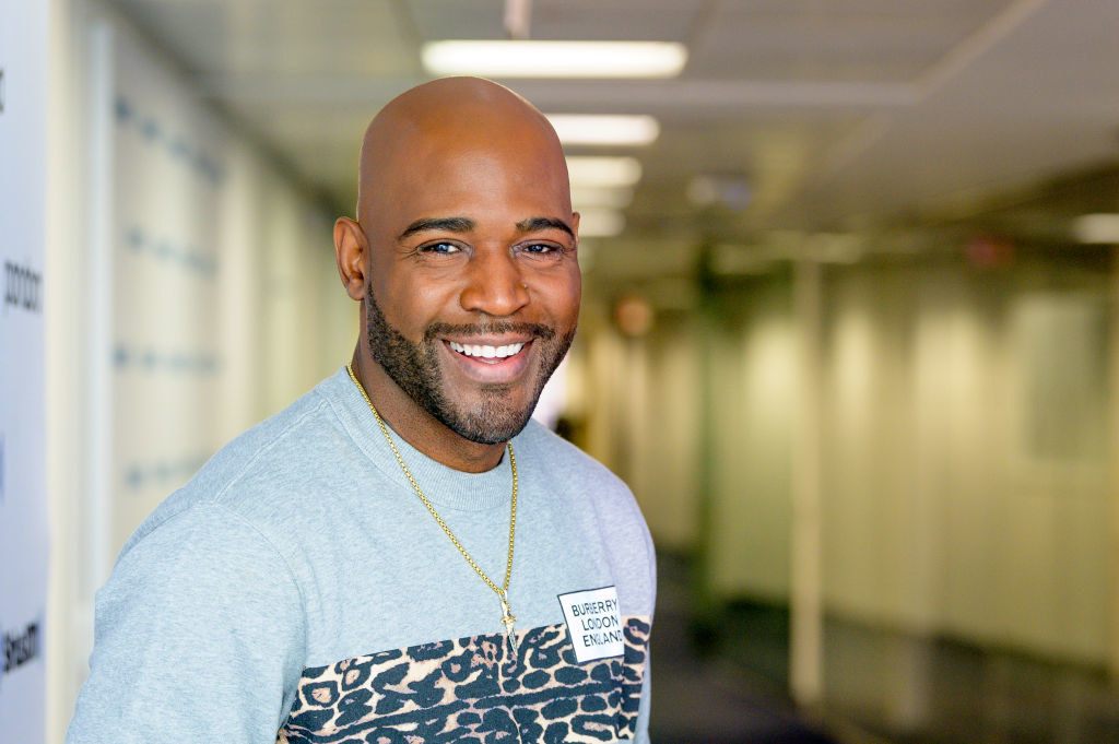 A smiling Karamo wearing a &quot;Burberry London England&quot; shirt and a necklace