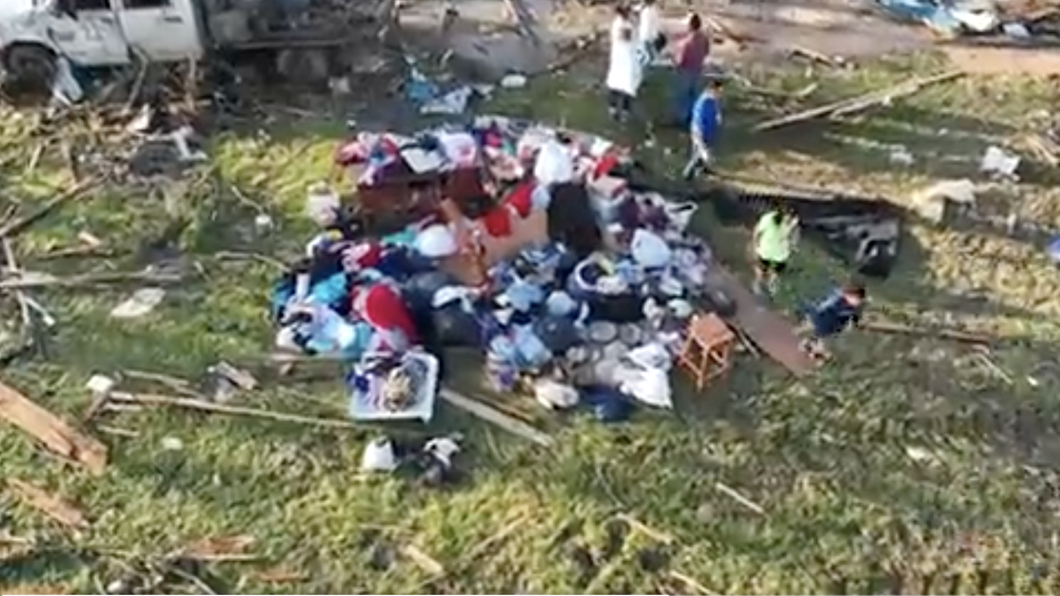 Overhead shot of people standing on the grass with their belongings amid debris