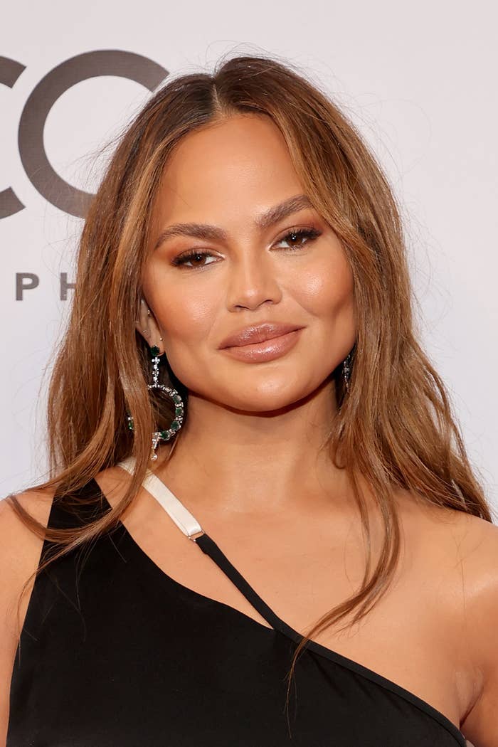 A close-up of Chrissy in a one-shoulder outfit and drop earrings