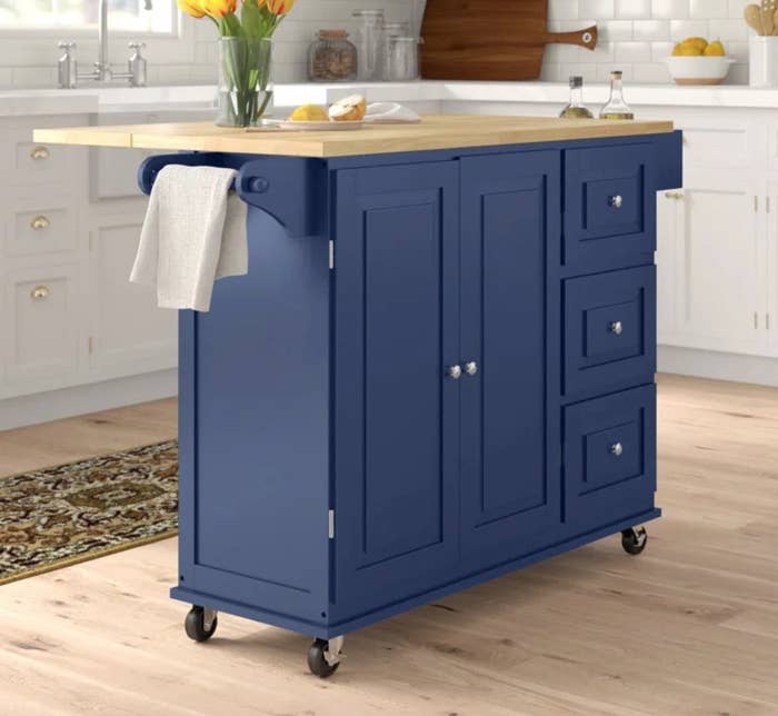the blue wheeled cart with a wooden top in a decorated kitchen