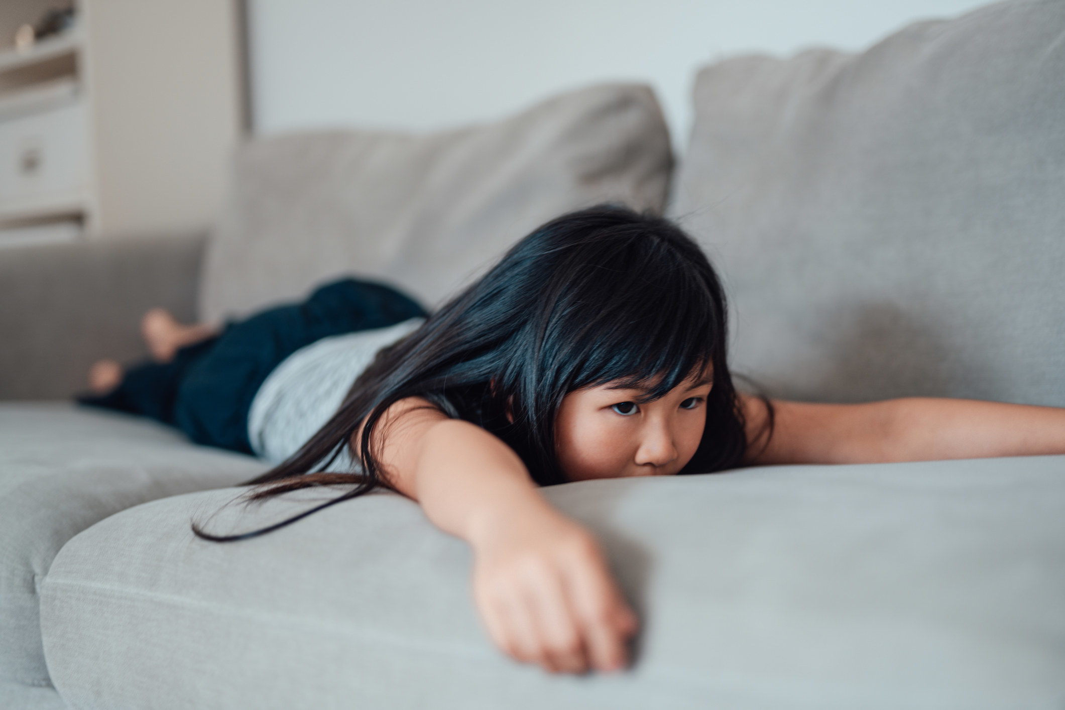 A girl lays on the couch looking upset.