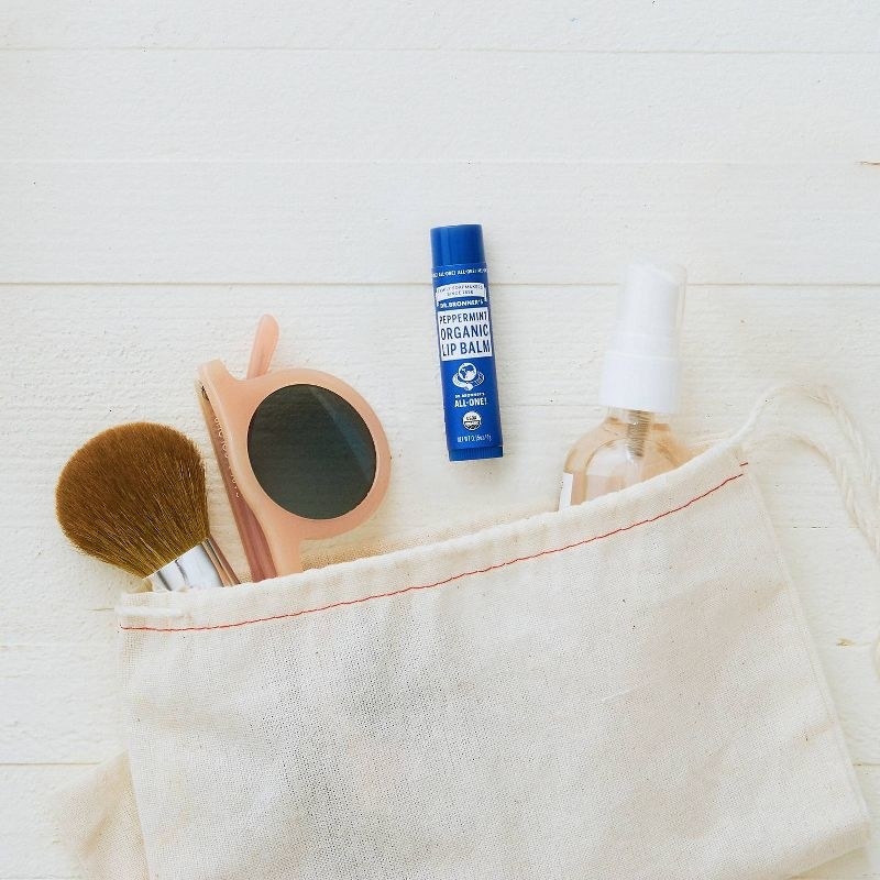 A bag with a makeup brush, sunglasses, a lip balm, and spray