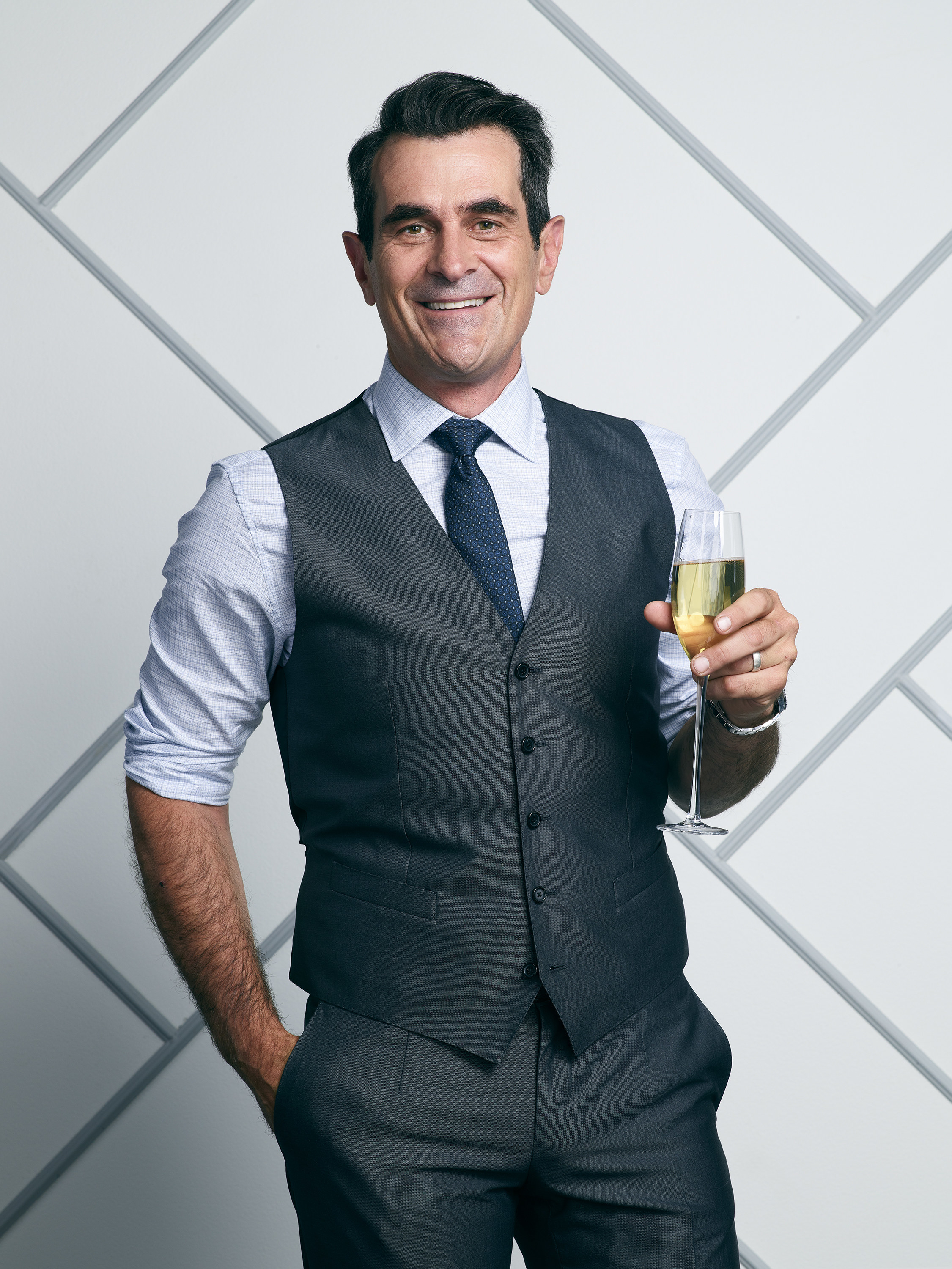 Ty in a vest and rolled-up sleeves, holding a champagne glass and smiling