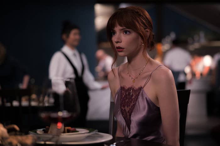 Anya Taylor-Joy sitting at a dining table in a scene from The Menu in a purple outfit